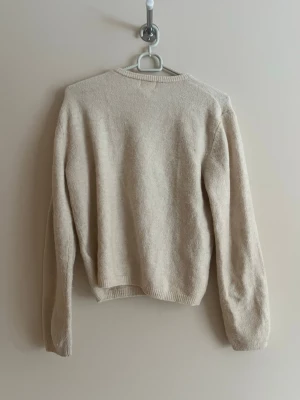 Beige kofta från H&M med knappar - Mysig beige kofta från H&M med rund halsringning och knäppning framtill. Koftan har långa ärmar och ribbade muddar vid ärmslut och nederkant. Perfekt att slänga över en t-shirt eller linne för en enkel och clean look.