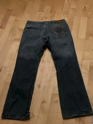 Mörkblå bootcut jeans med brodyr - Säljer ett par mörkblå bootcut jeans med snygg broderad detalj på ena bakfickan köpta i köpenhamn secondhand i somras . Klassisk femficksmodell med raka ben och låg midja. Jeansen är i denim och har en avslappnad passform, perfekta för en cool vardagslook.