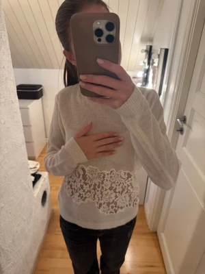Vit stickad tröja med spetsdetalj - Säljer en vit stickad tröja med lång ärm och bred spetsdetalj i midjan. Tröjan har rund halsringning och ribbade muddar vid ärmslut och nederkant. Materialet är mjukt och lätt.