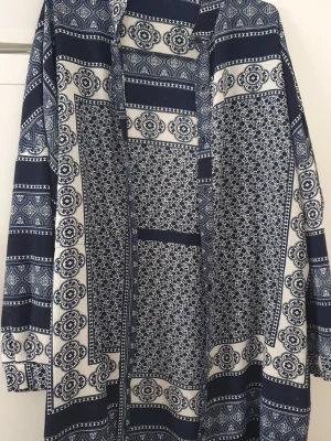 Klänning - Säljer en långklänning från Boohoo i marinblått och vitt med ett detaljerat rutigt och blommigt mönster. Klänningen har långa ärmar och en avslappnad passform, perfekt för dig som gillar bohemiska vibes och snygga prints. Lite nopprig.