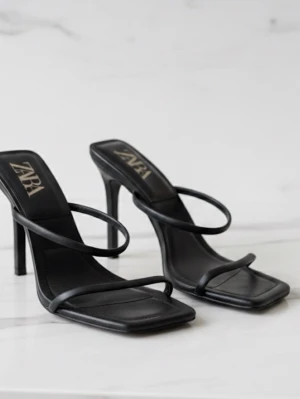 Svarta strappy sandaler från Zara - Stilrena svarta sandaler från Zara med tunna remmar och fyrkantig tå. Klackarna är höga och smala, vilket ger en elegant siluett. Tillverkade i konstläder med minimalistisk design och öppen häl. Perfekta för dig som gillar trendiga och moderna skor.