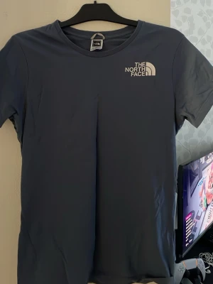 Blå t-shirt från The North Face - Snygg blå t-shirt från The North Face med klassisk logga tryckt på bröstet. T-shirten har rund halsringning och korta ärmar. Tillverkad i mjuk bomull som känns skön mot huden. Perfekt för en avslappnad och stilren look.