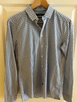 Rutig skjorta från tiger of sweden  - Klassisk rutig skjorta från tiger of sweden i blått och vitt. Skjortan har lång ärm, knappar framtill och en tidlös krage. Tillverkad i mjuk bomull som känns skön mot huden. Perfekt för en avslappnad men ändå stilsäker look.