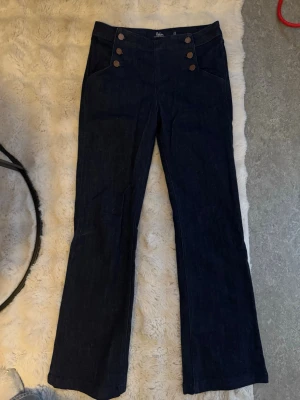 Mörkblå sailor jeans från Boden - Mörkblå jeans från Boden med hög midja och dekorativa guldknappar framtill i sailor-stil. Jeansen har raka ben och två framfickor. Tillverkade i klassiskt denimtyg som ger en tidlös look.