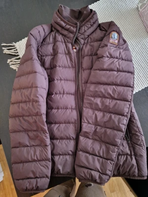Brun pufferjacka från Parajumpers - Snygg brun pufferjacka från Parajumpers med quiltad design och hög krage. Jackan har dragkedja framtill, logotyp på ärmen och ljus insida. Tillverkad i lätt och värmande material, perfekt för kalla dagar.