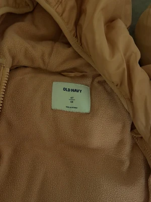 Ljusrosa pufferjacka Old Navy 4T - Ljusrosa pufferjacka från Old Navy i storlek 4T. Jackan har huva, dragkedja framtill och två sidofickor. Insidan är fodrad med mjuk fleece för extra värme. Perfekt för kalla vinterdagar och riktigt mysig att bära.