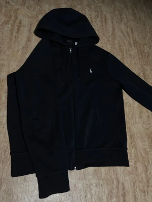 Ralph Lauren zip hoodie  - Säljer en svart zip hoddie från Ralph Lauren som är i mycket bra skick, som ny. Storlek M, Nypris 2300kr, mitt pris 899kr.                                         Hör av er för fler bilder eller vid funderingar!