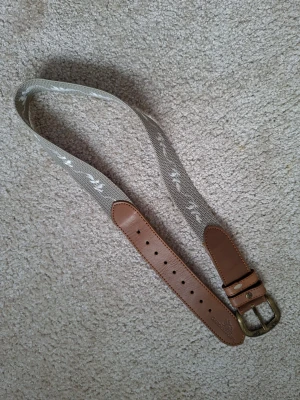 Skärp Garden Girl - Snyggt bälte från Garden Girl med beige textilband och bruna skinn-detaljer.