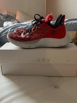 Under armour basketskor curry flow 9 - Säljer ett par röda Curry sneakers med svart och vitt mönster på ovandelen, svarta skosnören och en vit sula med svarta stänk. Skorna har meshmaterial för bra ventilation och en unik röd fluffig detalj på plösen. Perfekta för dig som gillar sportig och cool stil.