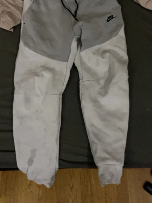 Nike tvåfärgade mjukisbyxor - Säljer ett par mjukisbyxor från Nike i tvåfärgad design med ljusgrå upptill och vit nedtill. Byxorna har resår i midjan och muddar vid bensluten. Tillverkade i mjukt material för maximal komfort. Perfekta för chill dagar eller träning.