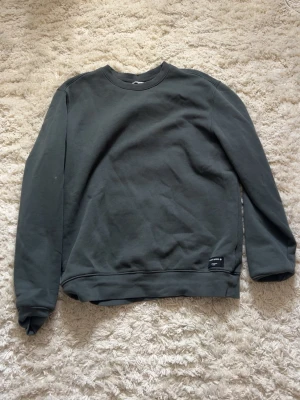 Mörkgrå/grön sweatshirt från Björn Borg - En stilren mörkgrå/grön sweatshirt från Björn Borg med rund halsringning och ribbade muddar. Tröjan har en diskret logotyp vid nederkanten och är tillverkad i mjukt bomullsmaterial. Perfekt för en avslappnad och trendig look. Har ingen lapp men aldrig använt.