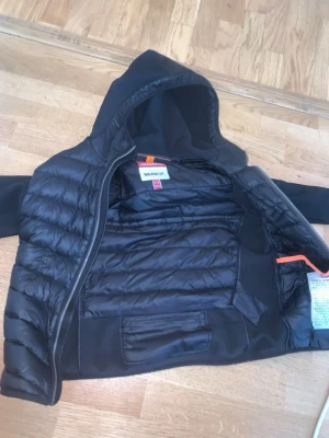 Svart dunväst med huva Parajumpers - Snygg svart dunjacka  från Parajumpers med huva och dragkedja. Jackan  har quiltad design och är lätt vadderad för extra värme. Perfekt för lager-på-lager och streetstyle. Märkesdetaljer på insidan. Klassisk och stilren look.