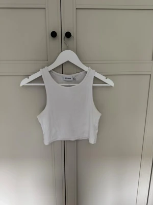 Vit ribbad linnetopp från Weekday - Säljer en vit ribbad linnetopp från Weekday i storlek M. Toppen är croppad och ärmlös med rund halsringning
