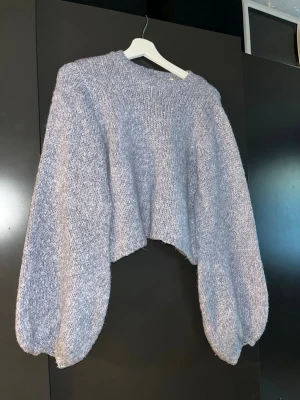 Blå/grå cropped stickad tröja - Säljer en ljusgrå stickad tröja med oversized ballongärmar och cropped passform. Tröjan har rund halsringning och är stickad i ett mjukt, fluffigt material som känns riktigt cozy. Perfekt för lager-på-lager och chill outfits. Storlek xxs men passar mig som har S också. 
