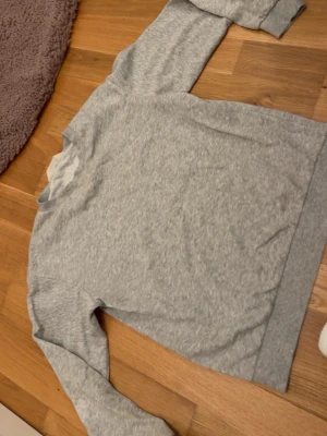 Grå sweatshirt från H&M - En basic grå sweatshirt från H&M i mjukt bomullsmaterial. Tröjan har rund halsringning, långa ärmar och ribbade muddar vid ärmslut och nederkant. Köpt för 349kr.