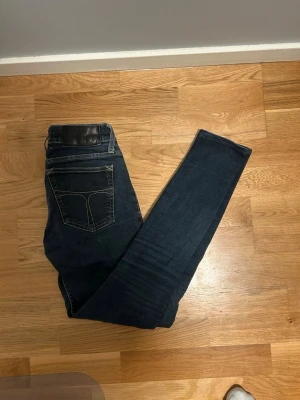 Mörkblå skinny jeans Tiger of Sweden - 28/32 - Säljer ett par mörkblå skinny jeans från Tiger of Sweden. Klassisk femficksmodell med guldfärgade detaljer och kontrastsömmar. Jeansen har låg midja och är tillverkade i stretchig denim för en tight passform.