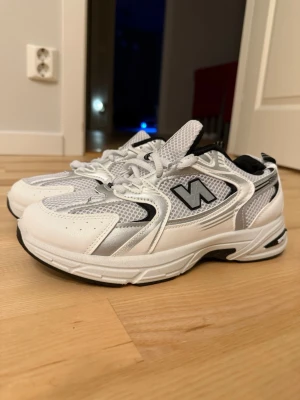 Vita sportiga sneakers med meshdetaljer - Fräscha vita sneakers med svarta och grå detaljer, meshpaneler för extra andningsförmåga och en chunky sula. Sidan pryds av ett N och texten 598. Perfekta för en sportig look och streetstyle.