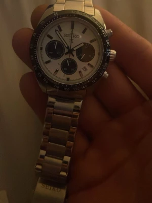 Seiko kronografklocka i silver - Stilren Seiko kronografklocka med vit urtavla, svarta detaljer och robust länkarmband i silverfärgat rostfritt stål. Klockan har flera subdials och tydliga indexmarkeringar, perfekt för dig som gillar klassisk och sportig design.