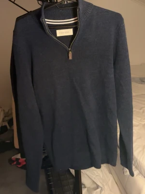 Mörkblå stickad tröja med halvzip - Mörkblå stickad tröja från Pier One med halvzip och ståkrage. Tröjan har långa ärmar och ribbade muddar vid hals, ärmslut och nederkant. Perfekt för lager-på-lager och enkel att matcha med jeans eller chinos.