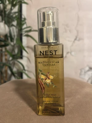 Nest Madagascar Vanilla Body Mist - Fräsch body mist från Nest i doften Madagascar Vanilla. Kommer i en genomskinlig fyrkantig plastflaska med pump och silverdetaljer. Innehåller närande baobabolja och har en varm, söt vaniljdoft. Perfekt för dig som älskar mjuka och exotiska dofter. Se bild hur mycket som är kvar 