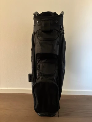 Svart golfbag från Callaway - Säljer en svart golfbag från Callaway med flera praktiska fickor och bärhandtag. Väskan är tillverkad i slitstarkt material och har tydlig Callaway-logga på sidan. Perfekt för att organisera och bära golfklubbor och tillbehör på banan.