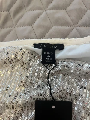 Silver paljettopp från Amisu - Glittrig silverfärgad topp från Amisu, täckt med paljetter för en riktigt festlig look. Modellen har långa ärmar och rund halsringning. Perfekt för dig som vill sticka ut och glänsa lite extra.