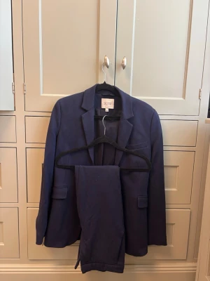 Mörkblå kostym från Dagmar - Snygg mörkblå kostym från Dagmar med klassisk kavaj och matchande byxor. Kavajen har slag, fickor med lock och en stilren passform. Perfekt för dig som vill ha en stilren och modern look.