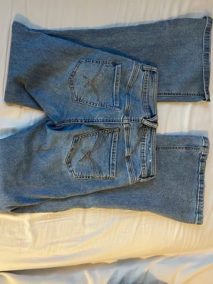 Blåa raka jeans från Garage - Säljer ett par klassiska blåa jeans från Garage Denim med raka ben och snygga bakfickor med dekorsömmar. Jeansen har hög midja och är tillverkade i slitstark denim. Perfekta för en avslappnad och trendig look.