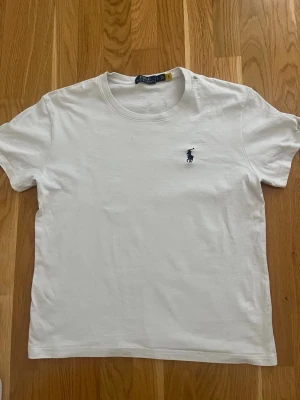 Vit t-shirt från Polo Ralph Lauren - Klassisk vit t-shirt från Polo Ralph Lauren med den ikoniska broderade loggan på bröstet. T-shirten har rund halsringning och korta ärmar, tillverkad i mjuk bomull för en skön och stilren look. Tröjan är i storlek S