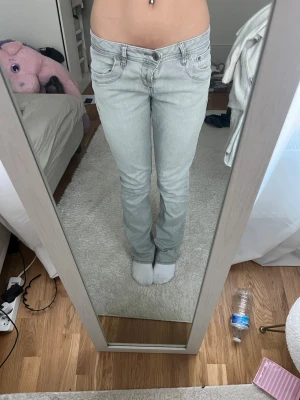 Ljusgrå bootcut jeans - Snygga ljusgrå bootcut jeans med klassisk femficksdesign och låg midja. Jeansen har diskreta sömmar och en stilren look som passar perfekt till en avslappnad stil. Tillverkade i denim med stretch för extra komfort. De har dessutom två stycken knappar eftersom de var för stora för mig.