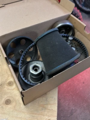 Remhjul och rem i svart metall - Säljer en låda med svarta remhjul och en svart rem, troligen till motor eller maskin. Delarna är av metall och gummi, med flera kugghjul och hjul med hål. Perfekt för dig som gillar att meka eller behöver reservdelar.