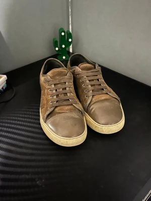 Bruna låga sneakers mocka - Snygga bruna sneakers i mocka med matchande bruna skosnören och tåparti i läder. Skorna har en vit sula och klassisk låg profil som passar till många olika stilar. Perfekta för dig som gillar en enkel men stilren look.