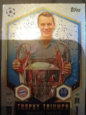 Trophy Triumph samlarkort Topps - Samlarkort från Topps med Trophy Triumph-tema, visar en spelare från FC Bayern München som håller Champions League-pokalen. Kortet har glittrig yta, silverdetaljer och klubbmärke. Perfekt för dig som gillar fotboll och samlar på sportkort.