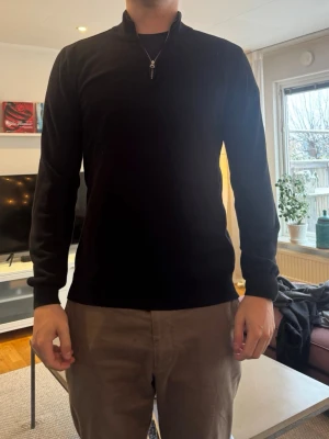 Svart halvzip tröja, John Henric - Snygg svart långärmad tröja med halv dragkedja i halsen. Tröjan har en clean och enkel design med ribbade muddar vid ärmslut och nederkant. Perfekt för dig som gillar stilrena plagg. Från John Henric i väldigt bra skick