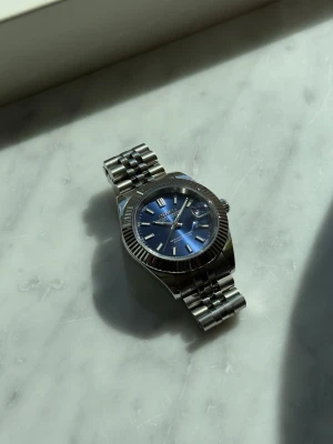 Handbyggd Seiko-mod – Datejust-inspirerad - Letar du efter något unikt på handleden? Här är den.  Blå sunburst-urtavla, fluted bezel och jubilee-armband i stål. Inspirerad av Datejust men till en bråkdel av priset. På baksidan kan du se urverket i rörelse genom det glasbottnet.  Aldrig använd, medföljer extra länkar och en fin klocklåda. Hör av dig om du har frågor eller vill ha fler bilder! 