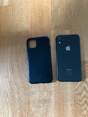 Svart iPhone XR med svart skal - Säljer en svart iPhone XR från Apple med stilren design och rundade kanter. Baksidan är i glas och ramen i aluminium. Medföljer ett svart mobilskal i mjukt material som skyddar mobilen. Perfekt för dig som vill ha en snygg och pålitlig smartphone.