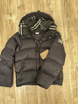 Burberry jacka - Säljer en svart pufferjacka från Burberry med avtagbara ärmar så den kan användas som väst. Kommer med tags. Storlek L men passar även M.