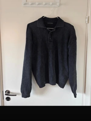 Mörkgrå stickad tröja från Zara - Mörkgrå stickad tröja från Zara med krage och knappar vid halsen. Tröjan har lång ärm och ribbade muddar vid ärmslut och nederkant. Perfekt för lager-på-lager och enkel att matcha med jeans eller chinos.