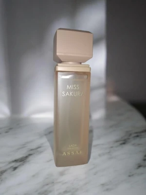 Miss Sakura parfym från Assaf - Miss Sakura parfym från Assaf med en stilren, fyrkantig flaska i frostat beige glas och matchande lock. Flaskan har guldtext och en modern design som känns lyxig och trendig. Perfekt för dig som gillar eleganta och minimalistiska doftflaskor.