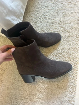 Bruna mocka stövletter med klack - Snygga bruna stövletter i mocka med bred klack och spetsig tå. Dragkedja på insidan för enkel påtagning. Perfekta till jeans eller klänning för en trendig look.