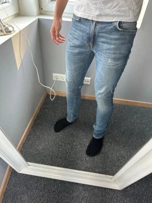 Lean dean nudie jeans - Säljer ett par ljusblå slim fit jeans från nudie. Jeansen har klassisk femficksdesign, normal midja och smal passform hela vägen ner. Materialet är stretchigt denim som ger en bekväm känsla och snygg siluett. Perfekta för en avslappnad och trendig look.