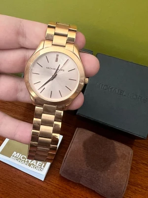 Klocka från Michael Kors i roséguld - Nästintill oanvänd damklocka från Michael Kors i roséguld  Fantastiskt fin klocka i roséguldpläterad metall som jag köpte när jag tänkte jag skulle bli en klockperson. Tyvärr blev jag aldrig det så denna har tyvärr legat oanvänd i sin låda.   33mm boett    Se bilder för skick. Fråga om du undrar något, jag är ingen erfaren klockperson så kan ha missat något!
