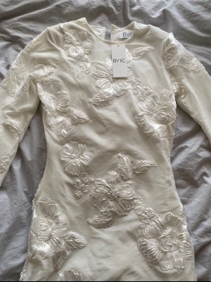Vit klänning - Superfin vit kort klänning som är långärmad och med en snygg figursydd passform! Perfekt till student! Klänningen har aldrig blivit använd och har fortfarande lappen kvar. Ordninarie pris är 930kr.