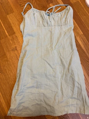 Ljusgrön klänning från BikBok - Söt ljusgrön klänning från BikBok med smala axelband och knytning framtill. Klänningen är kort och har en enkel, rak passform i ett mjukt linnematerial. Perfekt för varma dagar och enkel att styla med sneakers eller sandaler.