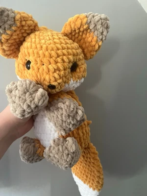 Handvirkad räv i mjuk plysch - Supergullig handvirkad räv i mjuk plysch med orange, grå och vit färg. Räven har stora öron, svans och svarta plastögon. Perfekt som dekoration eller mysig maskot. Gjord av tjockt garn som känns extra fluffigt och gosigt.