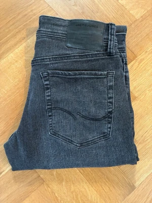 Mörkgrå jeans från Jack & Jones - Mörkgrå jeans från Jack & Jones i slim fit-modell med klassisk femficksdesign. Jeansen har en diskret broderad detalj på bakfickan och är gjorda i mjukt denim med stretch för skön passform.