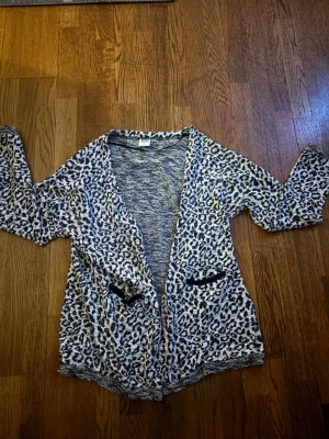 Leopardmönstrad kofta från Vero Moda - Snygg och mjuk kofta från Vero Moda i leopardmönster med svartvita toner. Koftan har två små fickor framtill med svarta detaljer och en avslappnad passform. 