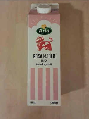 Arla rosa mjölk jordgubb 1L - En 1-liters förpackning rosa mjölk från Arla med smak av jordgubb. Kartongen är vit och rosa med en röd ko och grönt Arla-märke på framsidan. Innehåller 1% fett och har en klassisk skruvkork på toppen.