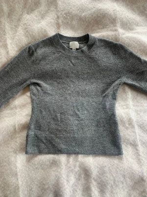 Grå stickad tröja med rund hals - Mysig grå stickad tröja från hm.  Ärmarna är lite utsvängda längst ned samt midjan på tröjan 