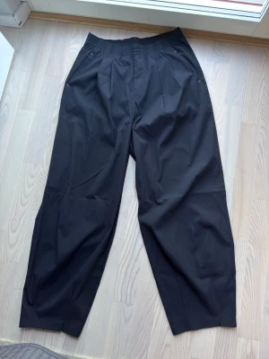 Svarta vida byxor från Under Armour - Svarta tränings/varfagliga byxor från Under Armour med bred resår i midjan och avslappnad, rak passform. Byxorna har diskreta sidfickor och är tillverkade i ett mjukt och ganska luftigt material som känns skönt mot huden. Perfekta för en chill och avslappnad stil. Byxorna är i storlek S med ganska baggy/loose passform. Nypris 1100 kr